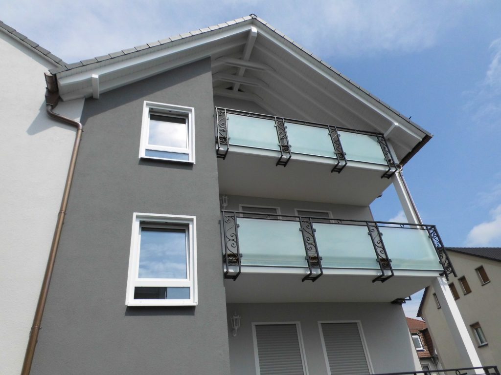 Graues Wohnhaus mit verputzter Fassade und Glasbalkonen